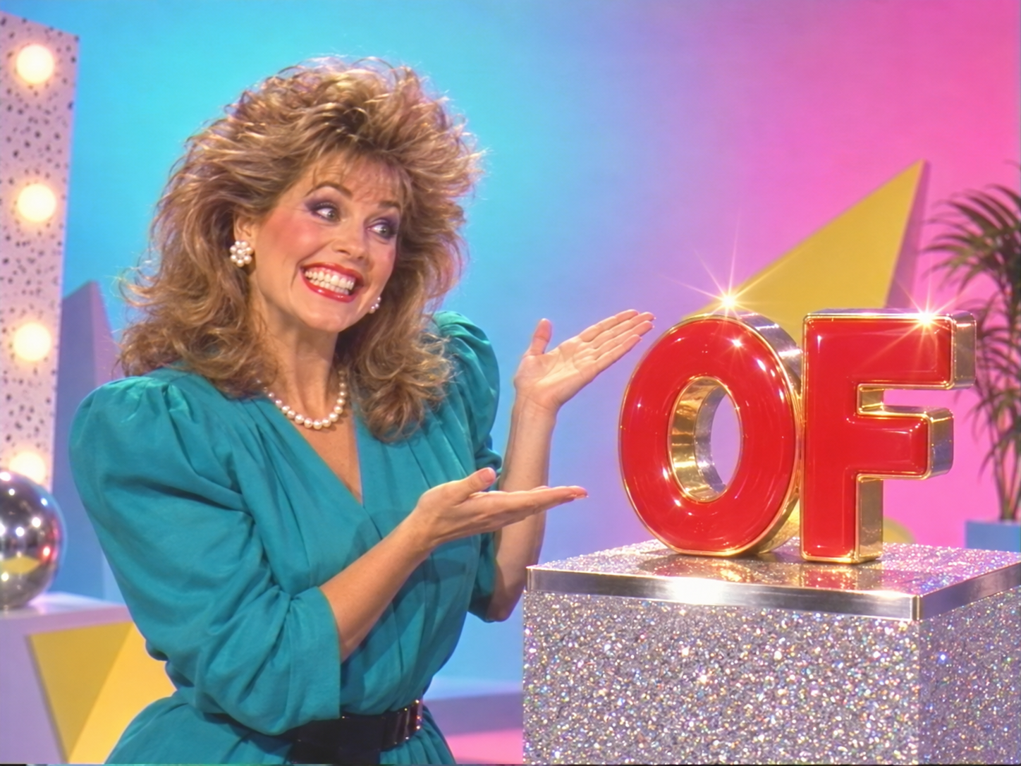 An extremely enthusiastic 1980s presenter gestures toward a shiny red OF object